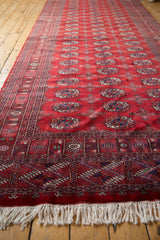 Angled view along a vintage Bokhara runner's red gul pattern and white end fringe.