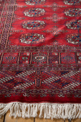 Detailed geometric end border and soft white fringe on a plush cherry-red Bokhara rug runner.