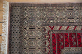 Detail of the vintage rug's corner shows the serpent border, silver and charcoal tones, and intact fringe.