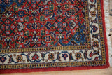 Corner of vintage Ardebil rug showing the full pile, intricate ivory border, and white fringe.
