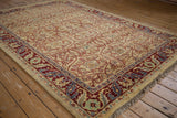 Angled view of the vintage carpet's corner, showing the red and blue scrolling leaf and palmette border.