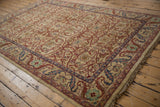 Angled view of a vintage Indian carpet's scrolling leaf border and floral lattice field.