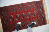 Top-down view of a vintage Bokhara rug runner shown for scale, highlighting its plush red pile.