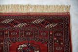 The secured end of a fine Bokhara rug, showing full ivory fringe and a geometric wool pile.