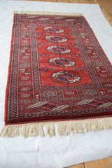 The traditional geometric design and plush wool pile of a vintage Bokhara rug from an angle.