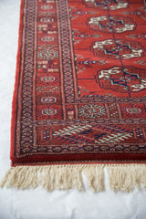 Intricate border, intact side selvage, and ivory fringe on a vintage red Bokhara rug runner.