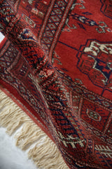 Full, plush wool pile of a vintage Bokhara rug, showing a soft fold and ivory fringe.
