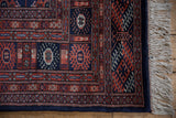 Corner detail of a vintage Bokhara rug with rust and navy geometric borders and ivory fringe.