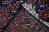 Corner detail of a vintage Bokhara rug showing the hand-knotted back, original side cord, and ivory fringe.
