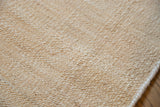 Hand-woven blanched amber jute rug texture showing its finished edge.