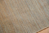 Hand-woven jute rug texture with natural beige, gray, and blue flecks.