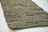 Clay rug's woven dark gray recycled leather and natural jute texture with a teal stitched edge.