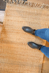 Hand-woven natural jute rug's textured surface, fringe, and feet.