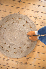 Hand-woven round jute rug, subtly grayed, showing coiled circles and natural texture.