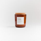 Orange and Clove soy candle in amber glass jar with white label and cork lid.
