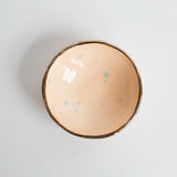 Peach handmade dish interior with blue speckles and a gold luster rim.