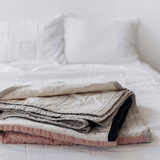 Folded Louise Gray quilt showing quilted cotton linen texture in flax, rose, black.