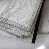 Folded Louise Gray quilt, embroidered L.G. logo, quilted ivory, flax, and black stripe.