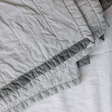 Louise Gray quilt with embroidered LG logo, light gray quilted texture, and dark gray trim.
