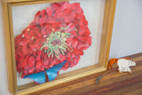 Gold shadow box frame housing the hand-arranged dark pink flower and blue butterfly.