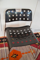 Black chair backrest and seat, showing perforated lacquered metal details.