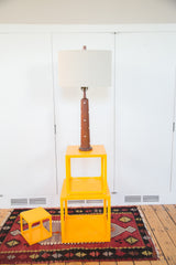 Martz Teak Lamp's inlaid wooden base on a stack of bright yellow cube tables.