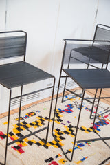 Black vintage Flyline barstool wire frame legs on a colorful patterned rug.