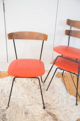 Stacked Mid Century Modern Clifford Pascoe chairs with chipped black iron legs and orange vinyl seats.