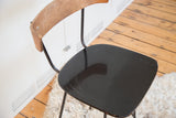Close-up of vintage Pascoe barstool's black vinyl seat with surface wear and wood back.