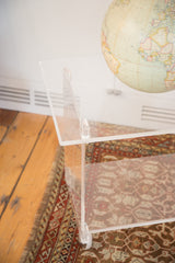 Vintage Lucite rolling cart corner showing clear acrylic, caster wheel, and surface marks.
