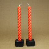Two vibrant orange-red rope taper candles in black square bases.