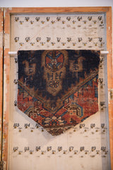 Rugling wall art made from a dark, geometric antique Kurdish rug fragment on a dowel.