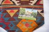 Vintage postcard pinned to an antique Turkish Kilim fragment; geometric red, blue, and yellow.