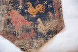 Corner detail of a circa 1910 Persian rug fragment with pictorial rooster designs and time-softened texture.