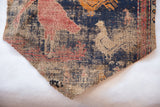 Stitched corner of an antique Persian rug fragment showing the coarse wool weave and tan rooster motif.