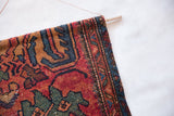 Vintage Lilihan rug fragment's rustic edge with wooden dowel and copper wire.