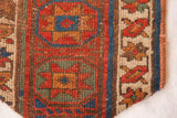 Hand-knotted antique Kurdish rug fragment showing geometric motifs in earthy red, blue, and brown.