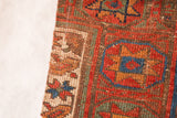 Stitched edge detail of antique Kurdish rug fragment in vibrant geometric design.