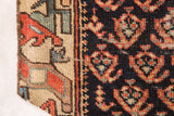 Hand-knotted antique rug fragment detail: beige geometric border, dark blue field with rust-red motifs.