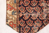 Detail of the antique Northwest Persian rug fragment, showing stylized red, navy patterns and beige geometric border.