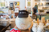 Black Rug Addict embroidered hat placed on top of a world globe.