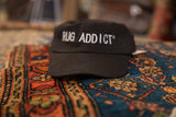 Black Rug Addict hat with white embroidery, resting on a colorful vintage rug.