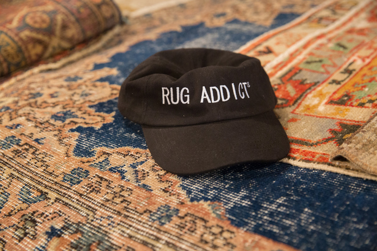Black cotton hat with "Rug Addict" embroidered in white block letters.