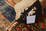 Detail of the adjustable back strap, metal buckle, and brand tag on a black Rug Addict hat.