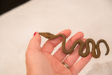 A hand holding the small vintage twisty iron snake to show its scale and handmade form.