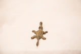 The aged, textured back of a small vintage bronze crocodile gold weight.