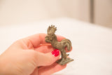 A small vintage rooster bronze gold weight held in hand, showing its textured patina.