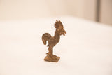 Side profile of a vintage rooster bronze gold weight showing detailed textural lines and patina.