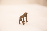 Vintage bronze monkey weight viewed from behind, highlighting the textured detail on its spine.
