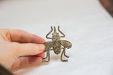 A vintage bronze fly gold weight held in hand to show its scale and patina.